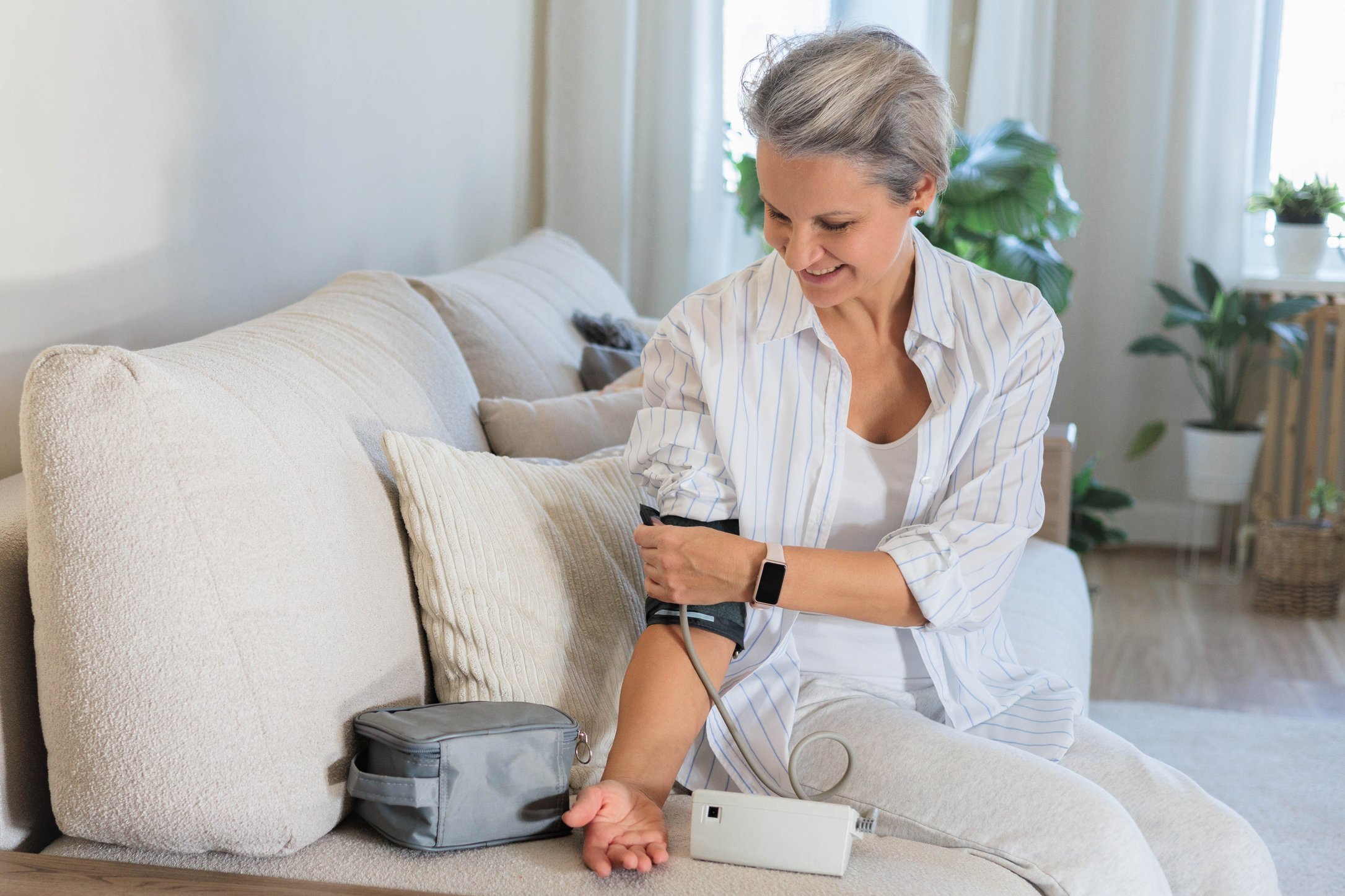 madura-hermosa-mujer-de-mediana-edad-con-cabello-gris-se-sienta-en-el-sofa-con-un-tonometro